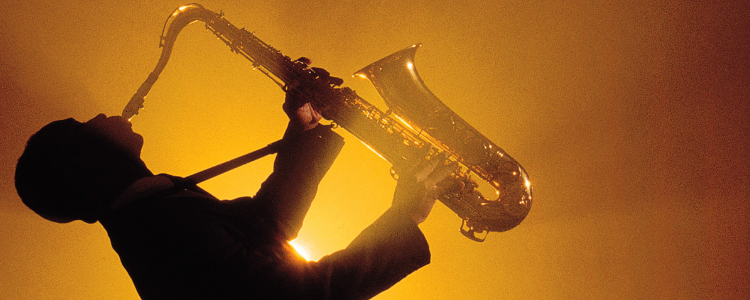 Imagem ilustrativa de um saxofonista tocando o saxofone com um fundo iluminado brilhante